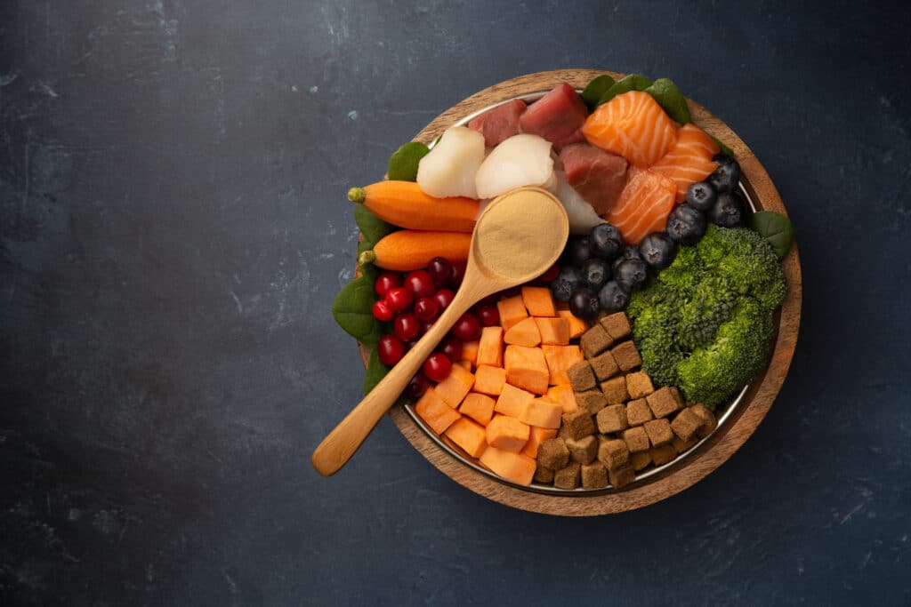 An image of fresh vegetables, fruit and raw salmon in a wooden bowl with a wooden spoon on top.