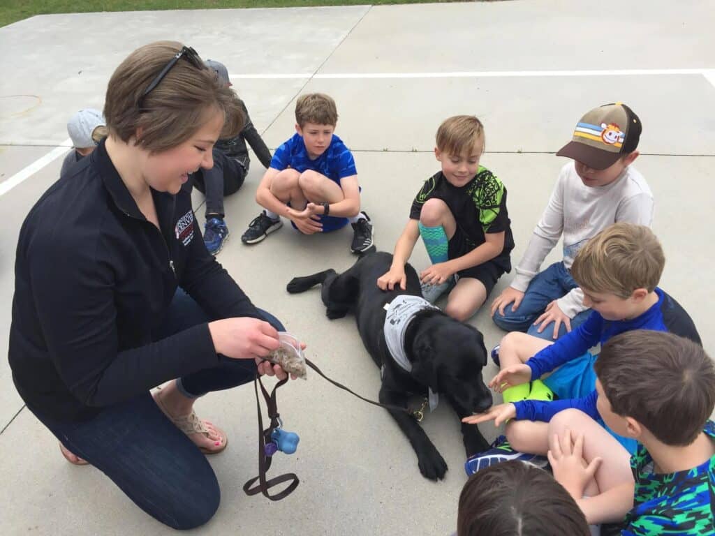 A woman introducing a black dog to a bunch of school children