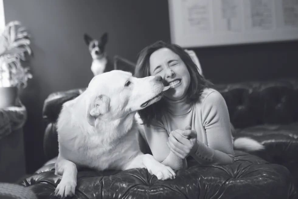 Black & White image of Victoria being kissed by a large white dog as a small dog looks on from behind - Love, Dog