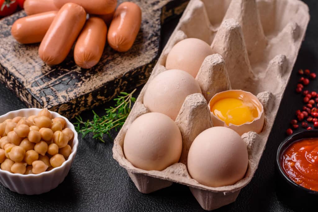 Raw chicken eggs in a box, cherry tomatoes, chickpeas, spices, salt and herbs. Ingredients for a delicious, nutritious breakfast